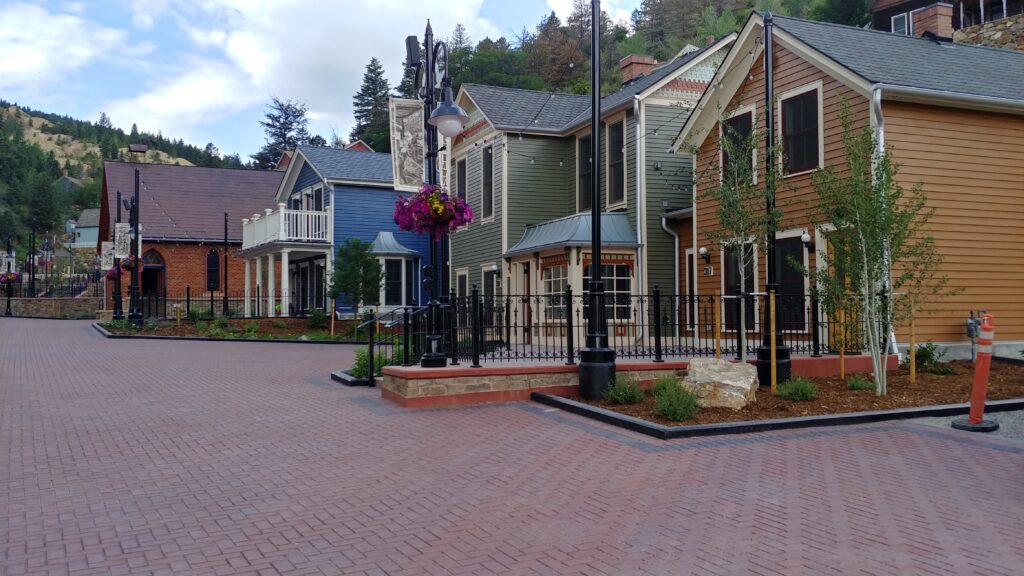 Historic district streetscape with restored colorful buildings, brick pedestrian plaza, decorative lighting, landscaping, and mountain town architecture