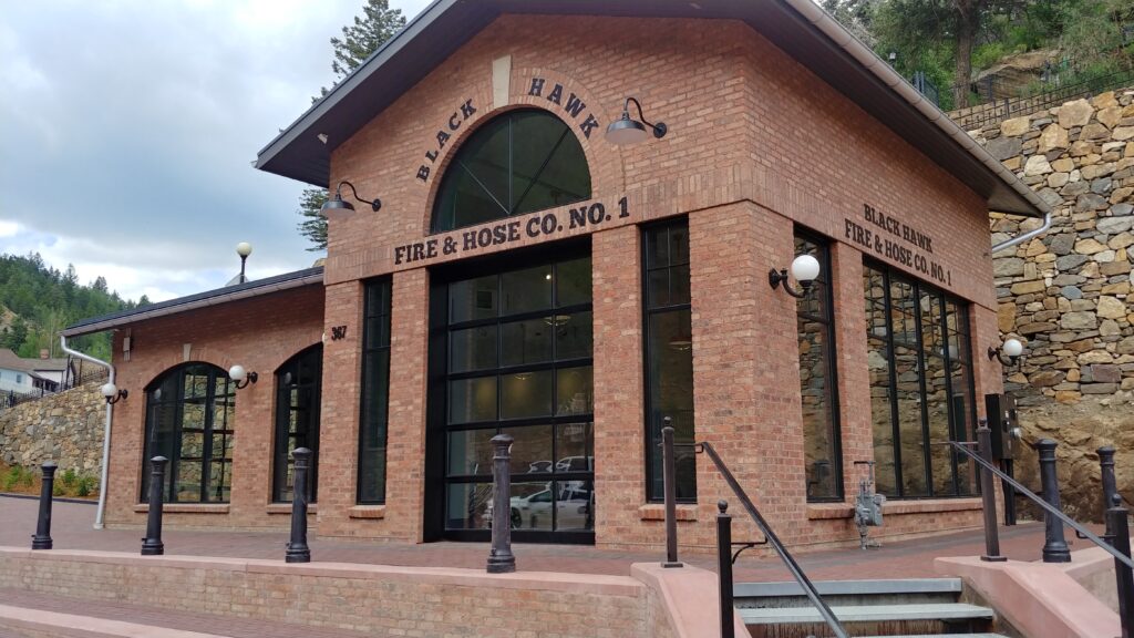 Restored historic fire station building with brick exterior, large glass garage doors, traditional signage, and pedestrian plaza design