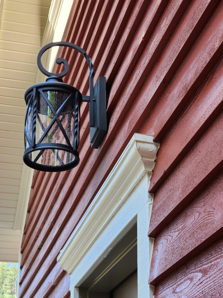 Close-up detail of a historic home exterior featuring red wood siding, white trim, and traditional black wall lantern lighting restored by PEH Architects