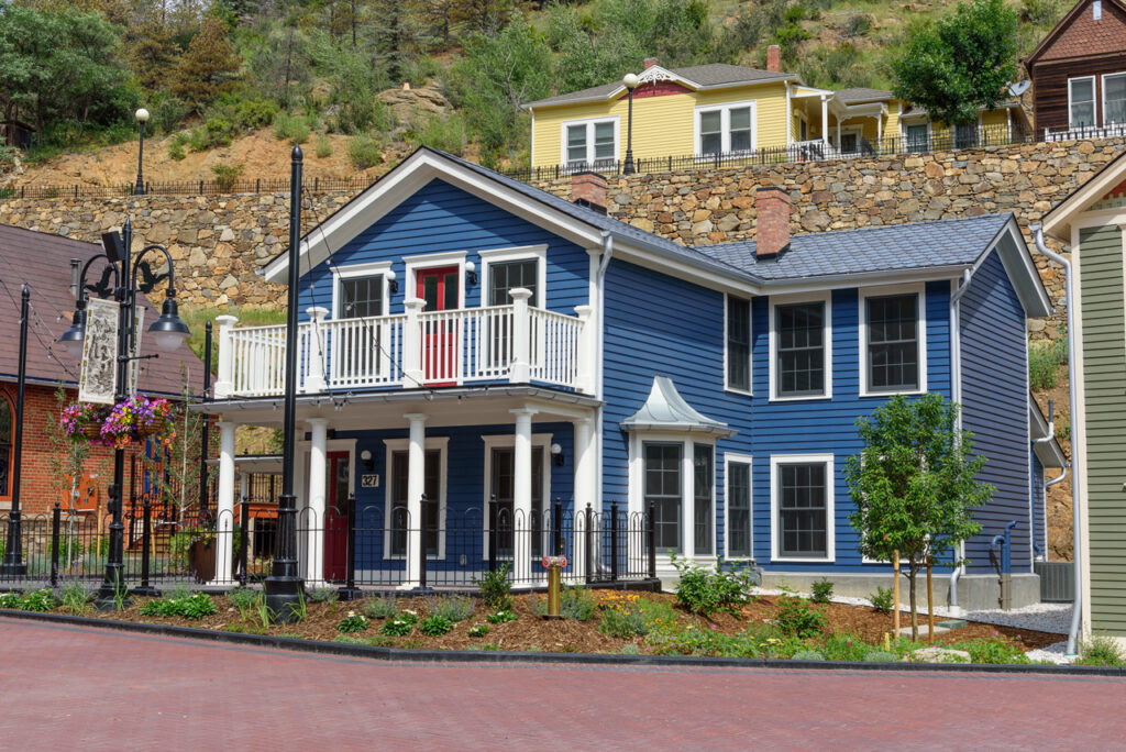 Restored historic blue building with traditional architecture, landscaped frontage, brick plaza, and mountain hillside surroundings