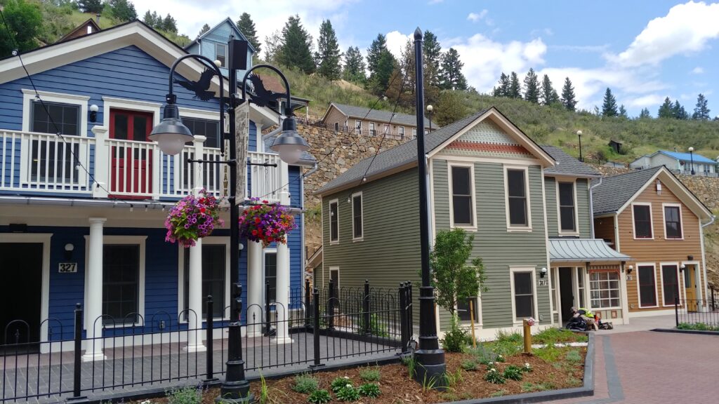 Historic-style residential buildings featuring colorful siding, covered porches, decorative trim, landscaped pathways, and traditional exterior design