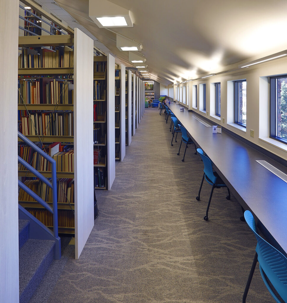 Modern library interior featuring custom bookshelves, long study tables, seating areas, windows, and contemporary architectural design by PEH Architects