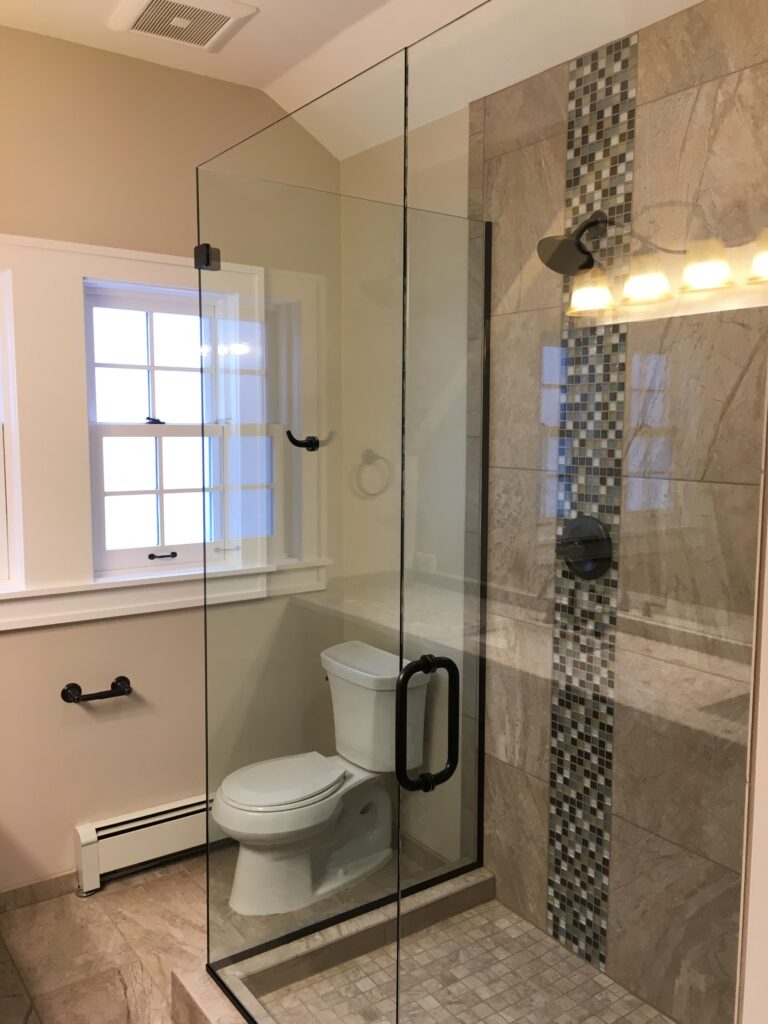 Modern bathroom renovation featuring a frameless glass shower enclosure, stone wall tiles, mosaic accent strip, and contemporary black shower fixtures