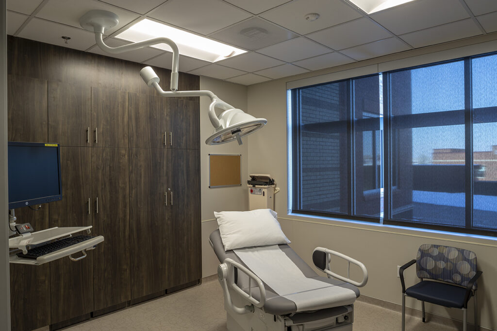 Modern healthcare examination room featuring medical equipment, patient bed, storage cabinets, and functional interior design