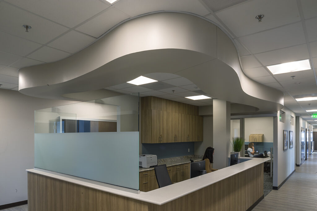 Modern healthcare reception area featuring curved ceiling design, reception desk, workstations, and contemporary medical facility interior