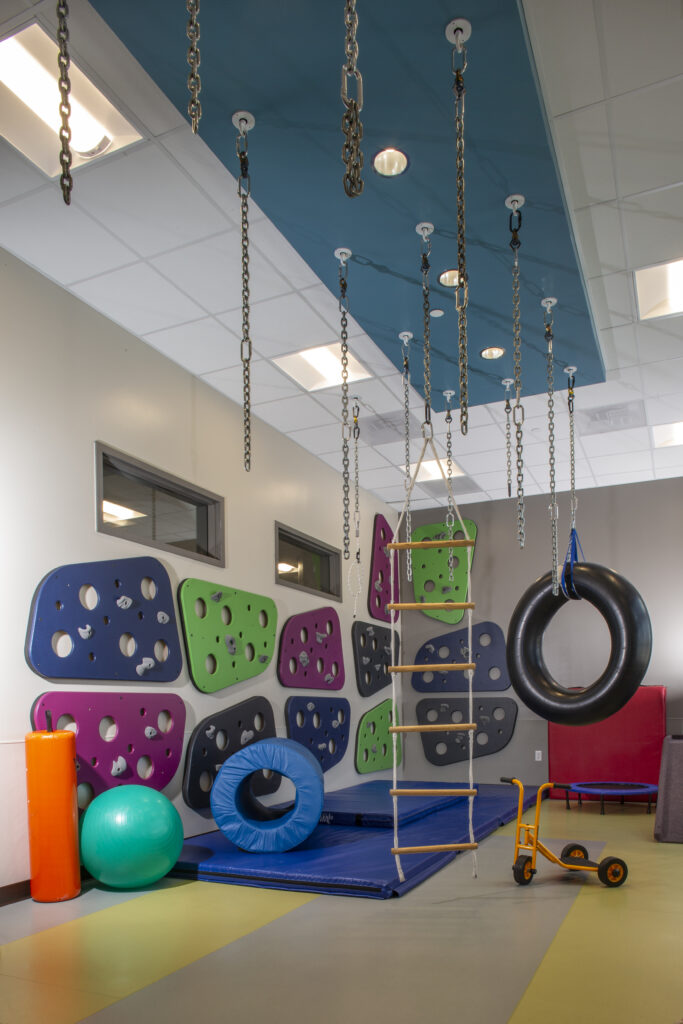 Colorful pediatric rehabilitation sensory gym with climbing walls, therapy swings, exercise equipment, and child-focused interior design