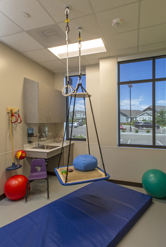 Pediatric rehabilitation therapy room with sensory swing, exercise equipment, therapy mats, and child-focused healthcare interior design