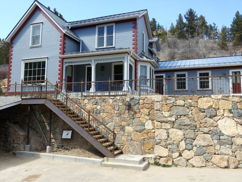 Residential home exterior featuring a covered porch, metal roof, stone retaining wall, exterior siding, and custom architectural details