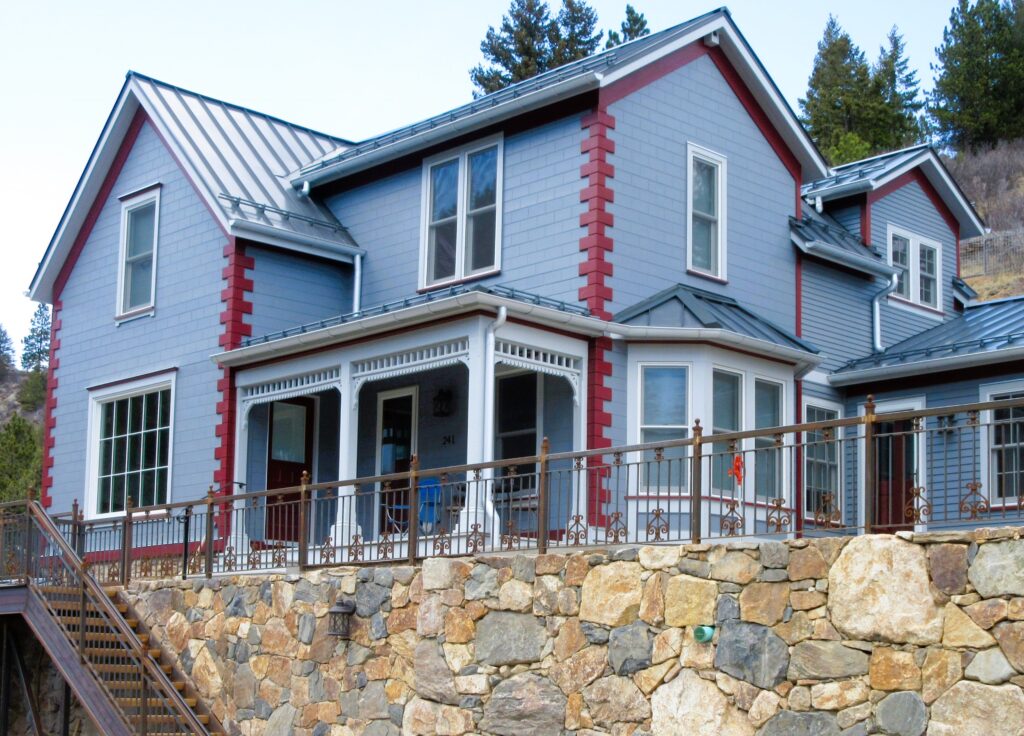 Residential home exterior featuring updated siding, metal roof, covered porch, stone retaining wall, and modern architectural details