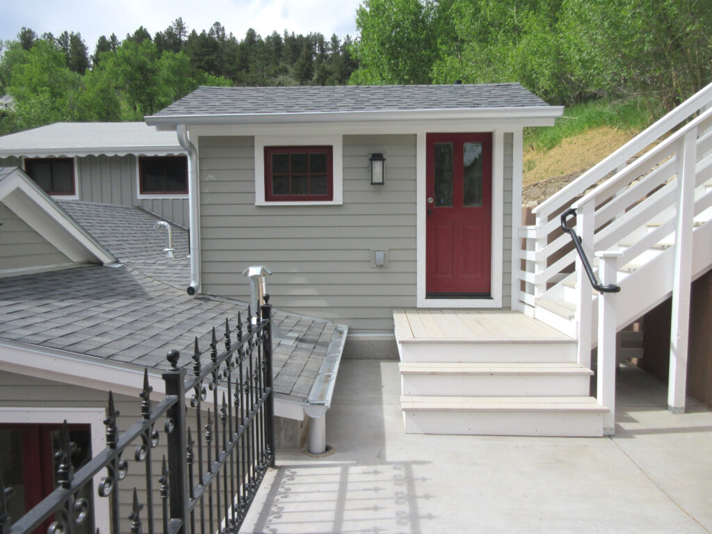 Residential exterior renovation featuring grey siding, white deck stairs, railing, and upgraded home entrance