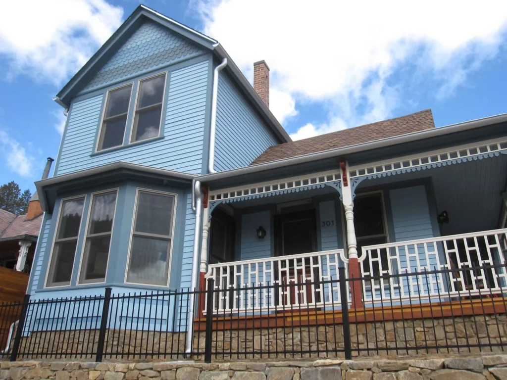 Historic Victorian home exterior with blue siding, white decorative trim, front porch railing, and stone foundation renovation