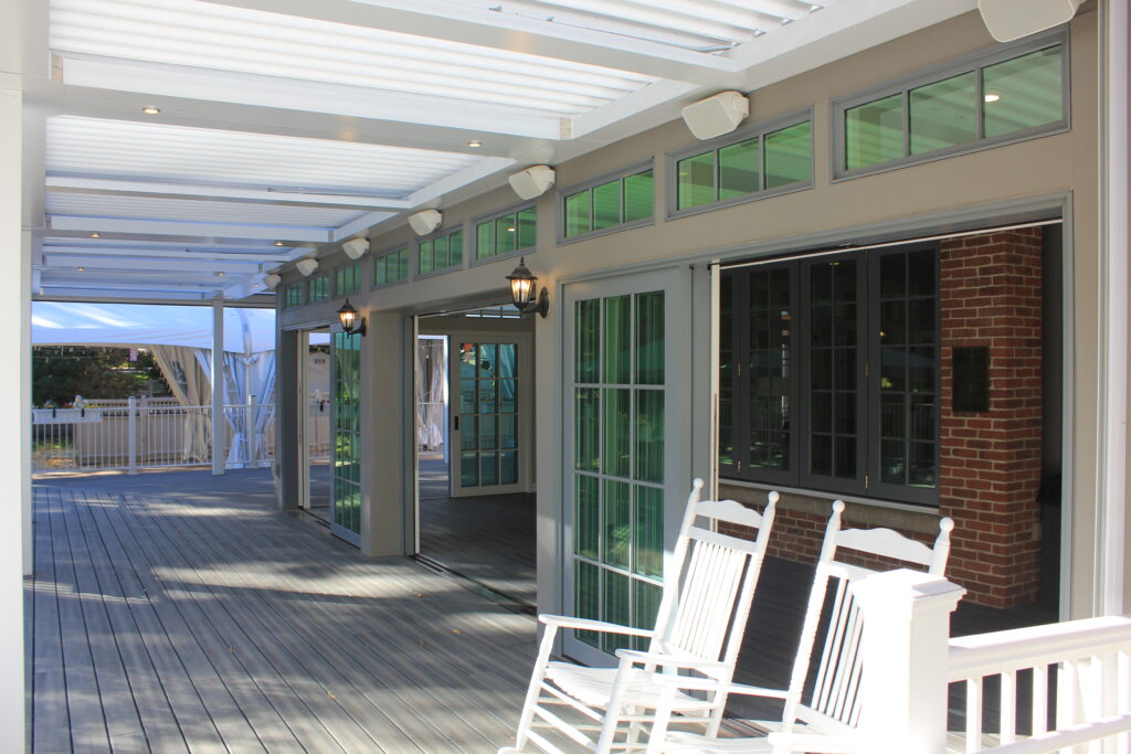 Covered outdoor patio with wooden deck, glass doors, pergola roof, and seating area for outdoor living