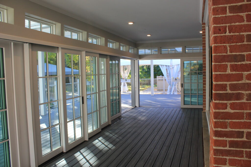 Modern enclosed deck area with glass folding doors, wooden flooring, and covered outdoor living space
