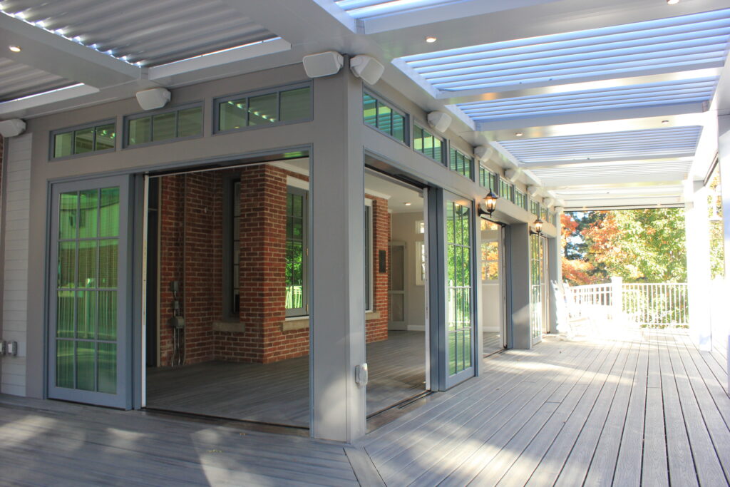 Modern covered deck with aluminum pergola roof, composite flooring, glass doors, and outdoor living space attached to brick home
