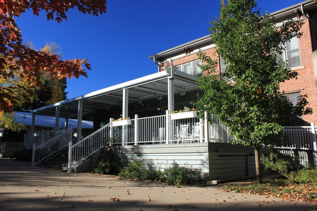 Residential covered deck with aluminum patio roof, white railings, stairs, and outdoor living area beside brick home